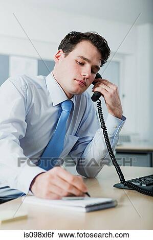 Stock Image - Office worker on telephone call, writing in notebook. Fotosearch