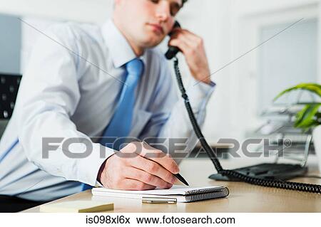 Stock Photo - Office worker on telephone call, writing in notebook. Fotosearch