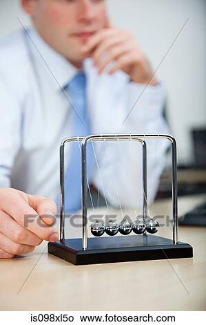 Office worker playing with newtons cradle View Large Photo Image Picture - Office worker playing with newtons cradle. Fotosearch