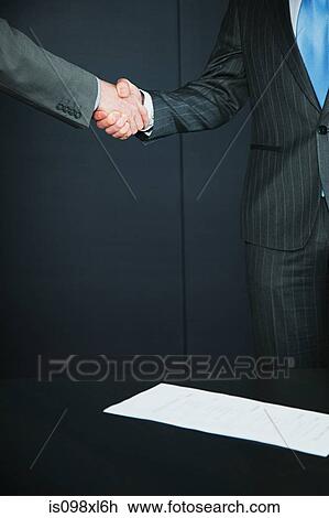 Stock Image - Two businessmen shaking hands at job interview. Fotosearch