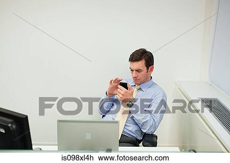 Stock Image - Businessman using smartphone in office. Fotosearch