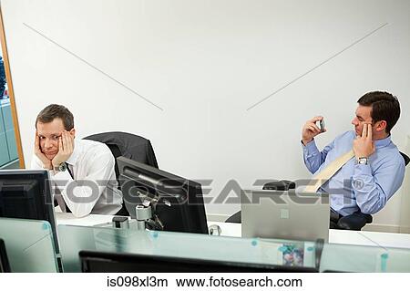Businessman using smartphone, male colleague looking sideways View Large Photo Image Picture - Businessman using smartphone, male colleague looking sideways. Fotosearch