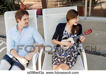 Couple sitting on lounge chairs, woman playing ukelele View Large Photo Image Stock Image - Couple sitting on lounge chairs, woman playing ukelele. Fotosearch