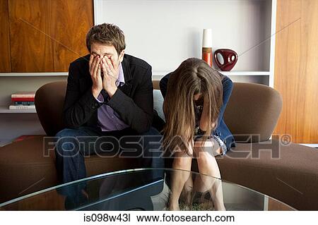 Stock Image - Couple sitting on sofa, man with head in hands. Fotosearch