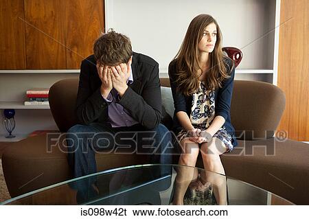 Couple sitting on sofa, man with head in hands View Large Photo Image Stock Photograph - Couple sitting on sofa, man with head in hands. Fotosearch