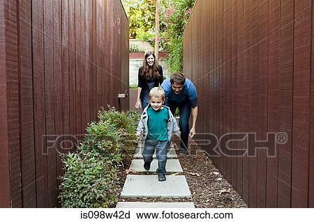 Stock Image - Parents watching young son running down path. Fotosearch