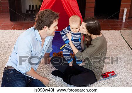 Stock Image - Parents with baby son sitting on living room floor. Fotosearch
