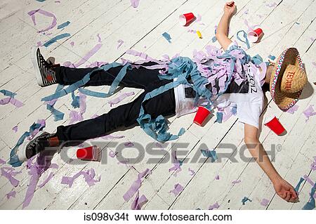 Stock Photograph - Man lying on floorboard covered with streamers at party. Fotosearch