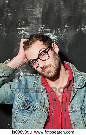 Stock Photograph - Man wearing denim jacket scratching head at party. Fotosearch