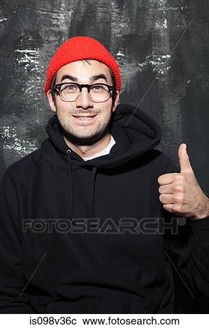 Stock Image - Man wearing red knit hat with thumbs up at party. Fotosearch