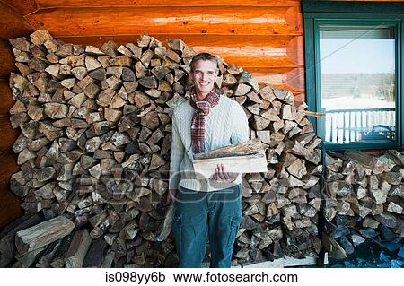 Stock Image - Man holding logs, portrait. Fotosearch