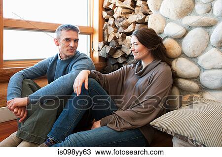 Stock Image - Mid adult couple sitting in log cabin. Fotosearch