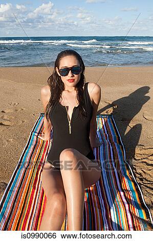 Stock Photograph - Woman sitting on beach towel. Fotosearch