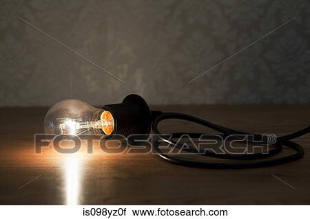Stock Image - Illuminated lightbulb on table. Fotosearch