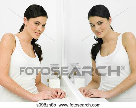 Stock Image - Reflection of young woman in bathroom mirror. Fotosearch
