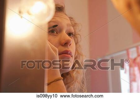 Stock Image - Teenage girl applying mascara in mirror. Fotosearch