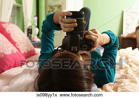 Stock Photo - Teenage girl lying on bed holding camera. Fotosearch