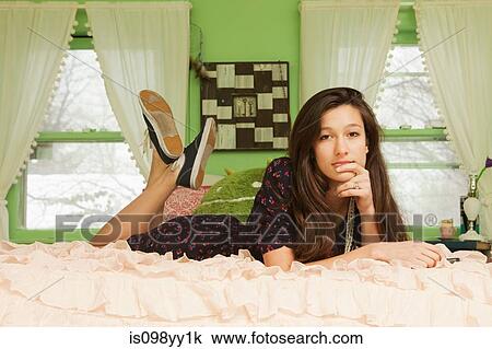 Stock Image - Teenage girl lying on bed, portrait. Fotosearch