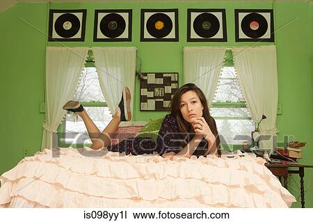 Stock Image - Teenage girl lying on bed, portrait. Fotosearch