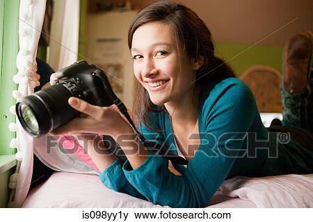 Teenage girl lying on bed with camera, portrait View Large Photo Image Stock Photo - Teenage girl lying on bed with camera, portrait. Fotosearch