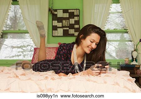 Teenage girl lying on bed with smartphone View Large Photo Image Picture - Teenage girl lying on bed with smartphone. Fotosearch