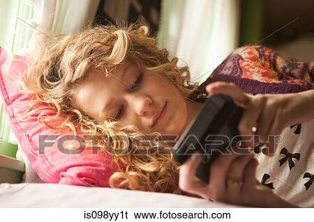 Teenage girl lying on bed with smartphone View Large Photo Image Stock Photograph - Teenage girl lying on bed with smartphone. Fotosearch