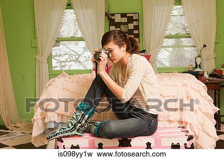 Stock Photo - Teenage girl sitting on bed taking photograph. Fotosearch
