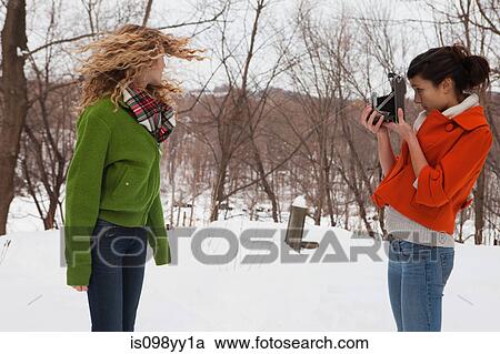 Stock Image - Teenage girl taking photograph of friend in snow. Fotosearch