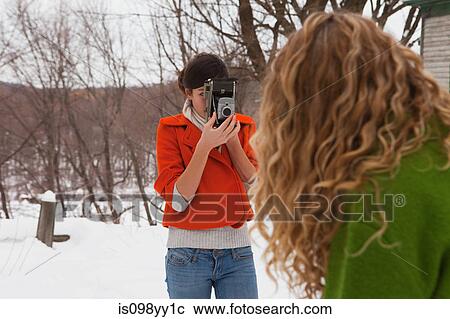 Stock Image - Teenage girl taking photograph of friend in snow. Fotosearch