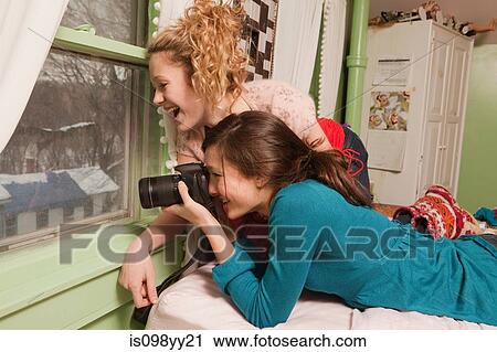 Stock Image - Teenage girls looking through window taking photograph. Fotosearch
