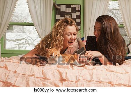 Picture - Teenage girls lying on bed with smartphone. Fotosearch