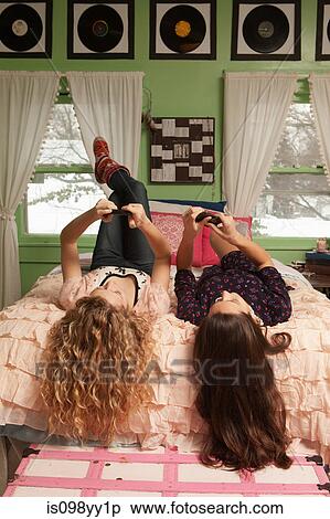 Stock Photography - Teenage girls lying on bed with smartphones. Fotosearch