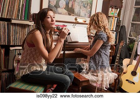 Stock Image - Teenage girls playing piano and singling. Fotosearch