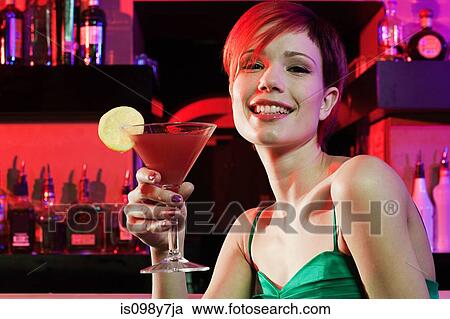 Stock Image - Happy young woman sitting at cocktail bar. Fotosearch