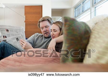 Couple sitting on sofa reading newspaper View Large Photo Image Stock Photo - Couple sitting on sofa reading newspaper. Fotosearch