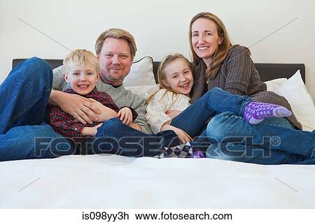 Stock Image - Family sitting on bed, portrait. Fotosearch
