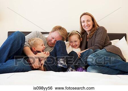 Stock Photograph - Family sitting on bed, portrait. Fotosearch