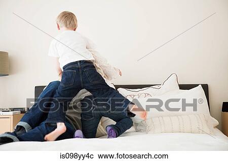 Stock Image - Father with two children playing on bed. Fotosearch