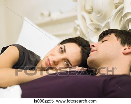 Stock Photography - Young couple lying in bed, woman's head on man's shoulder. Fotosearch