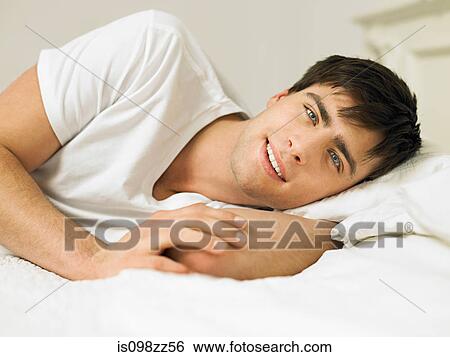 Young man lying on bed, portrait View Large Photo Image Stock Photograph - Young man lying on bed, portrait. Fotosearch