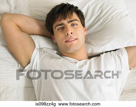 Young man lying on bed with hands behind head, portrait View Large Photo Image Stock Image - Young man lying on bed with hands behind head, portrait. Fotosearch