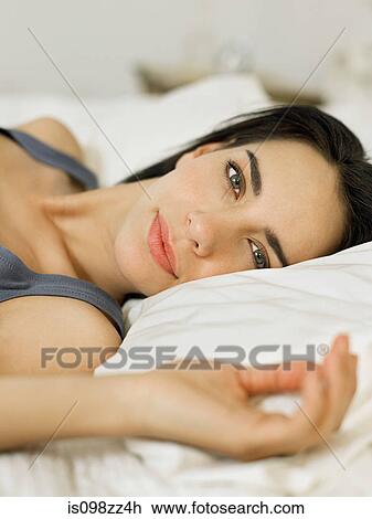 Stock Image - Young woman lying on bed, portrait. Fotosearch