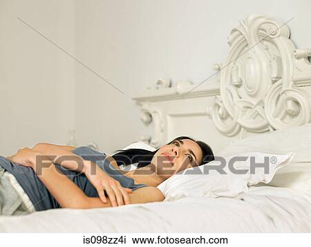 Stock Image - Young woman lying on bed. Fotosearch