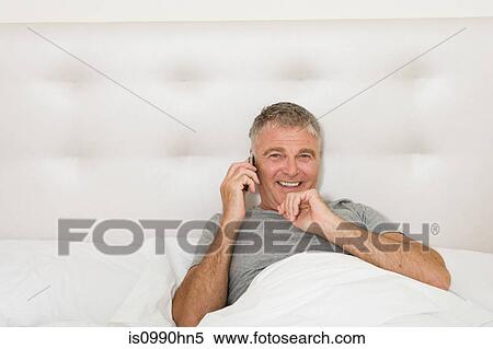 Man in bed on cellphone View Large Photo Image Stock Photography - Man in bed on cellphone. Fotosearch
