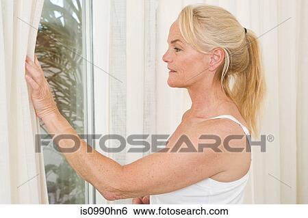 Mature woman opening curtains View Large Photo Image Stock Photograph - Mature woman opening curtains. Fotosearch