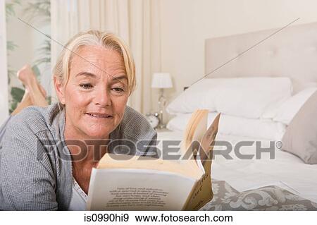 Stock Photo - Mature woman reading in bedroom. Fotosearch