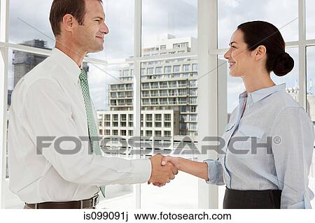 Stock Image - Businessman and businesswoman shaking hands in office. Fotosearch