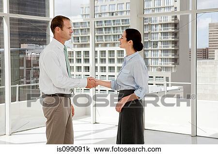 Stock Image - Businessman and businesswoman shaking hands in office. Fotosearch
