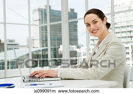 Picture - Businesswoman using laptop in office. Fotosearch