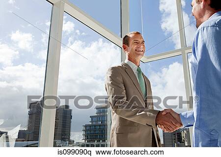 Stock Photography - Two businessmen shaking hands in office. Fotosearch